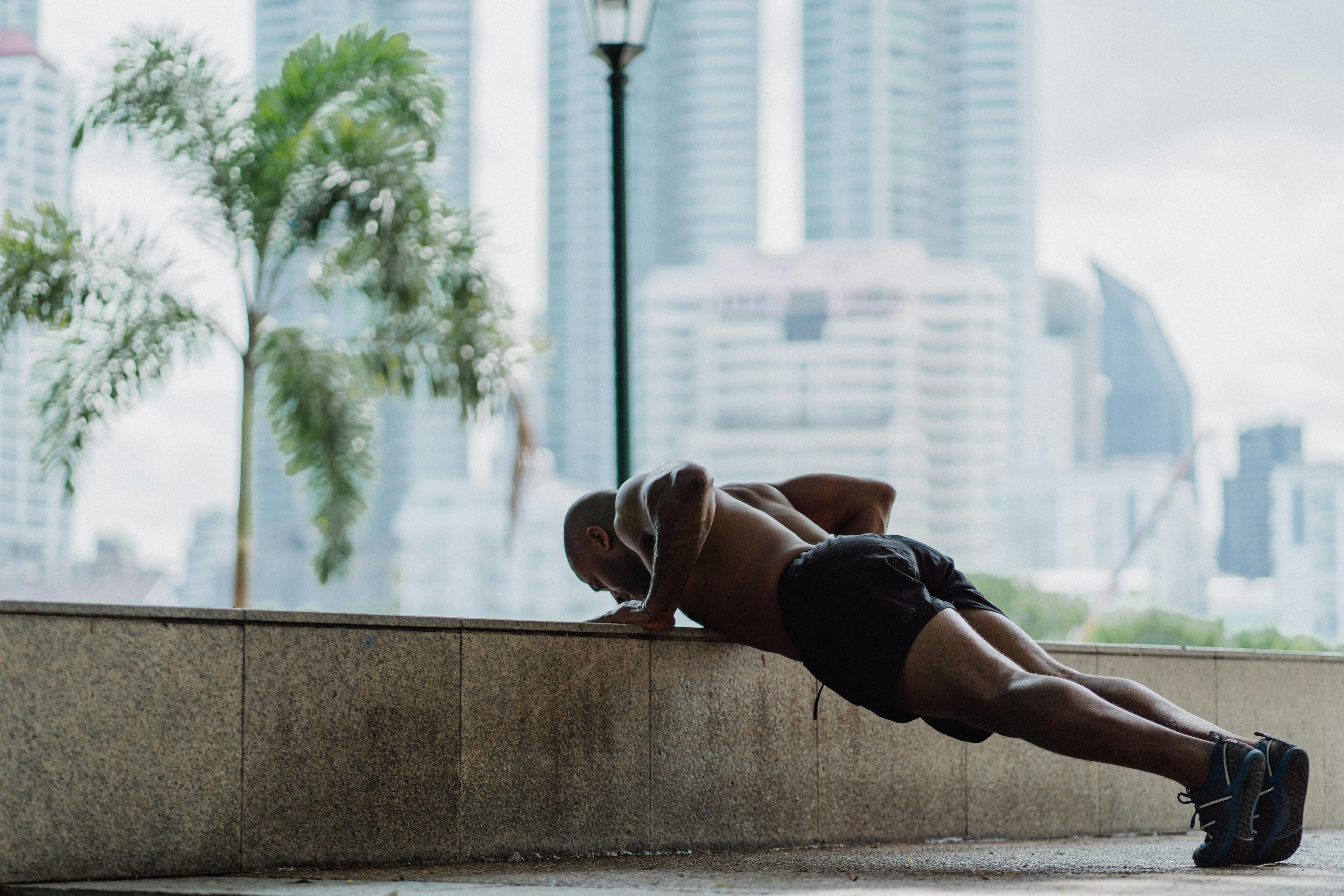 Strong man exercises outdoors, performing push-ups against a concrete wall.